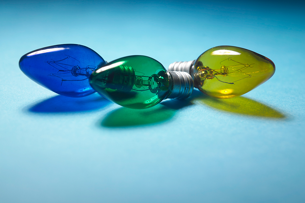 Close-up of three coloured light bulbs in blue, green and yellow lying on a blue background.