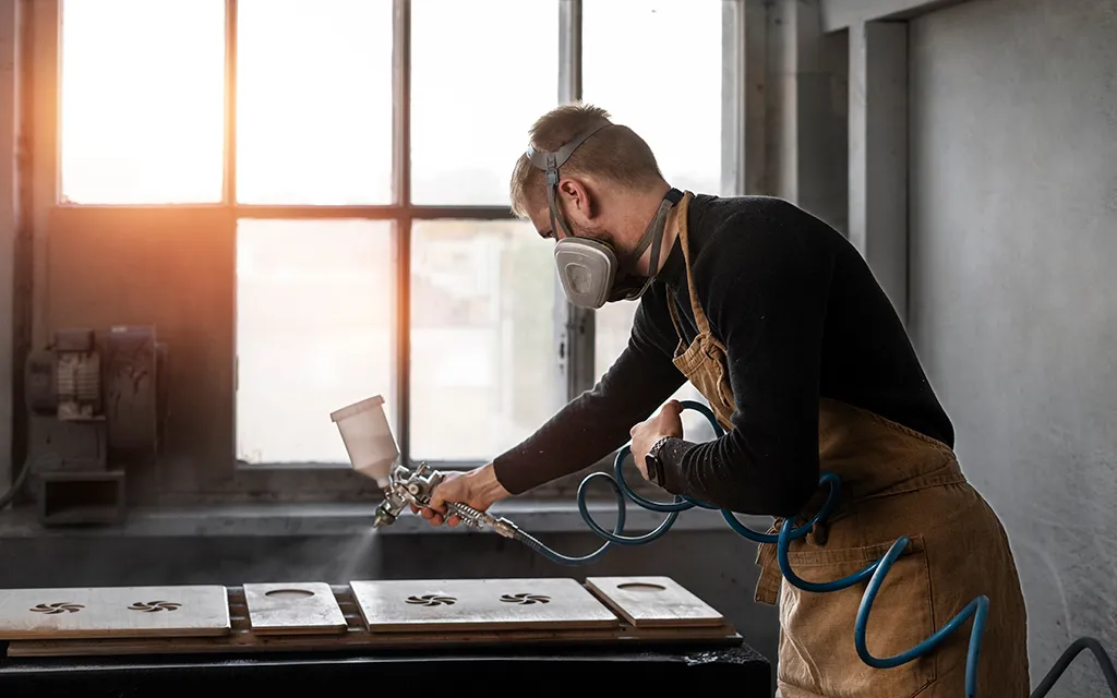 Craftsman applying a spray coating to wooden panels in a workshop